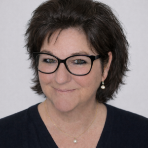 Porträtt av Carin Sigeskog, grundare av AiCarinDesign, med glasögon och mörkt kort hår, fotograferad mot ljus bakgrund.